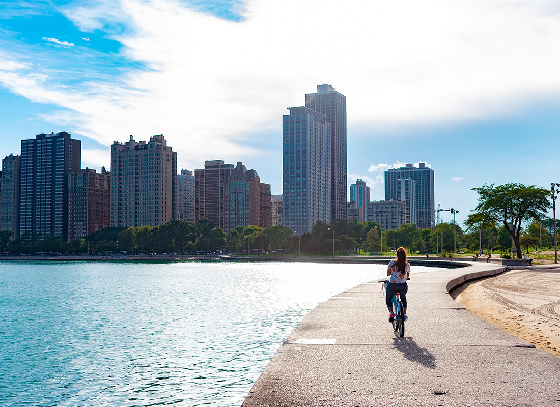 Employee Benefits - Woman Riding Bike Along Lake Michigan Towards the Sun in Chicago